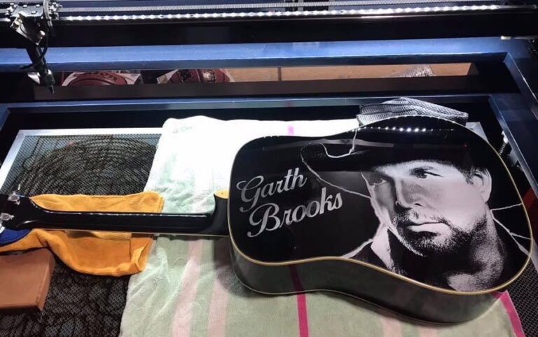 A black acoustic guitar engraved with a detailed portrait of country music star Garth Brooks, along with his name in elegant script, created using an AP Lazer® machine.